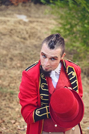 High angle of man in fancy red suit showing hat and looking at camera during performance in park