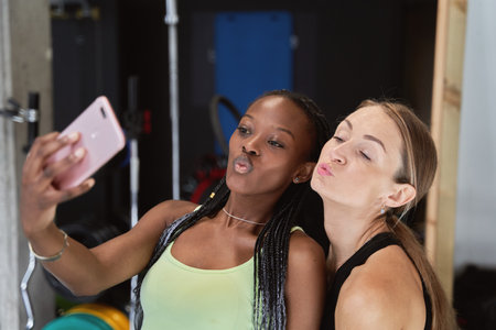 two fitness friends taking a happy selfie with their mobile phone after training at the gym