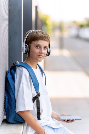 Teenage boy with backpack using mobile phone and headphones while relaxing on the street. Technology concept.の写真素材