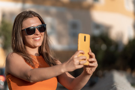 Woman in sunglasses taking photos with mobile phone outdoors on a sunny day. Technology concept.の写真素材