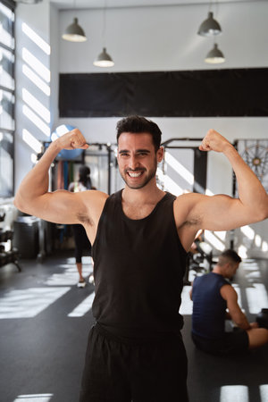 Fitness man showing his arm muscles while posing at the gym. Sports concept.