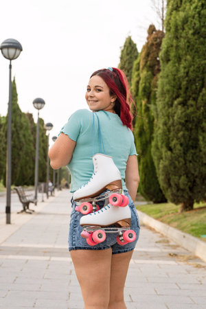 Roller skater woman with red hair on her back with her skates on her shoulder smiling and looking at...
