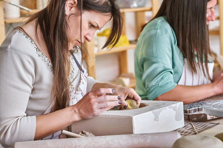 Woman working with clay while making a pottery craft in a workshop. Hobby and craft concept.の写真素材
