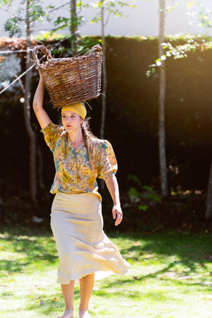 Young woman smiling while walking in her garden carrying a basket on her head.の写真素材