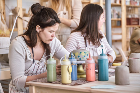 Female potter painting a handmade ceramic craft in a pottery workshop. Hobby and craft concept.の写真素材