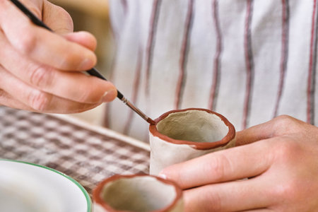 Close-up of a potters hands meticulously painting the edge of handmade ceramic cups with a fine brushの写真素材