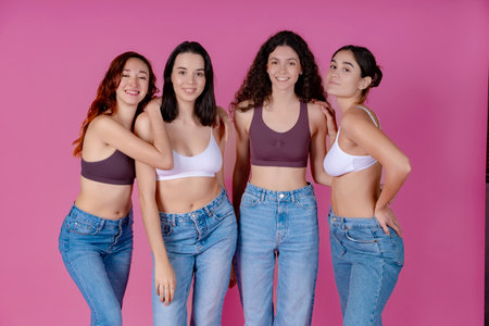 Four women in denim jeans radiate confidence and body positivity, standing together against a pink toneの写真素材