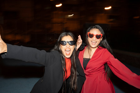 Two friends exude happiness during a fun night out, captured in motion with trendy heart-shaped...