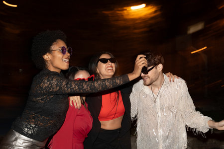 Laughing friends hugging and dancing on a city night with warm lighting.の写真素材