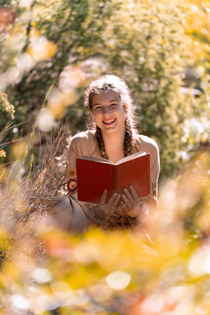 Happy young man smiling while reading a book outdoors in nature in a sunny day.の写真素材