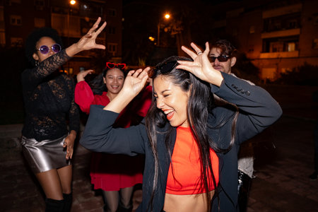 A spirited group of friends laugh and dance on a city street at night, enjoying each others company.