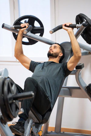 Concentrated man engaged in a chest press exercise at a modern gym during a workout session.の写真素材