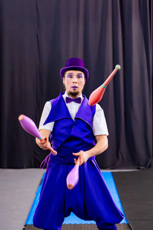 Juggler wearing purple costume and make up juggling clubs on a stage with black curtainsの写真素材