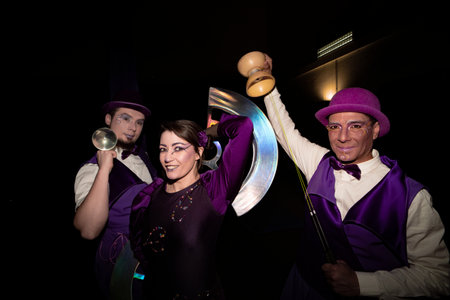 Three circus performers in purple costumes holding juggling props, posing together against a black backdropの写真素材