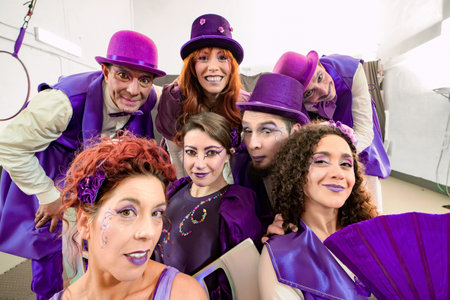 Group of smiling circus performers wearing purple costumes and makeup posing together for a backstage photoの写真素材