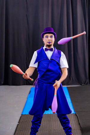 Male artist juggling colorful clubs, wearing a vibrant purple costume and top hat, showcasing skillful performance artの写真素材