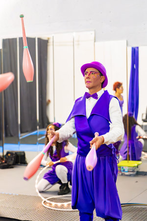 Male juggler practicing juggling clubs in a training room, with other performers in the backgroundの写真素材