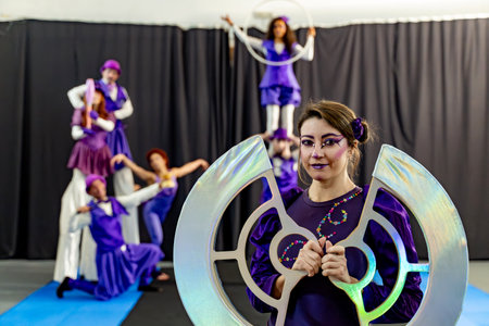 Circus performers in purple costumes rehearsing stilt walking, acrobatics, and hula hooping, with an iridescent prop in the foregroundの写真素材