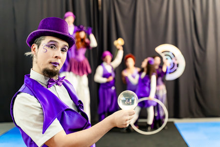 Magician wearing purple costume and top hat holding crystal ball with circus performers juggling and balancing in backgroundの写真素材