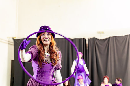 Redhead woman wearing purple costume and hat, spinning plastic hula hoop during circus rehearsalの写真素材