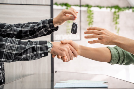 Two businessmen shaking hands after signing a car sale contract, with car keys being deliveredの写真素材