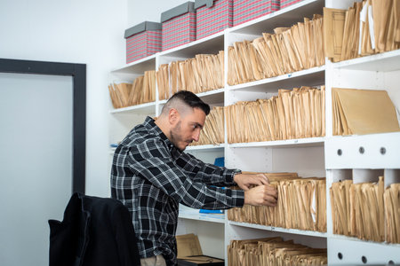 Office worker searching through files in an archive room filled with shelves of documents, ensuring efficient organization and retrieval of informationの写真素材
