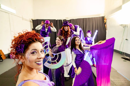 Redhead circus artist with purple makeup smiling and posing with her performing arts troupe in purple costumesの写真素材