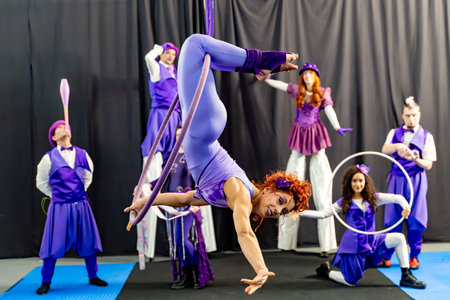Redhead acrobat performing on an aerial hoop, surrounded by juggling and balancing circus artists, highlighting teamwork and artistryの写真素材