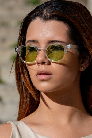 Young woman with long brown hair wearing stylish sunglasses and casual clothing, enjoying a sunny day outdoorsの写真素材