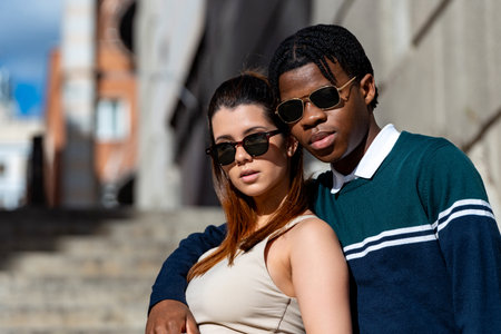 Interracial couple wearing stylish sunglasses, posing together on city steps, exuding love and happiness in a trendy urban settingの写真素材