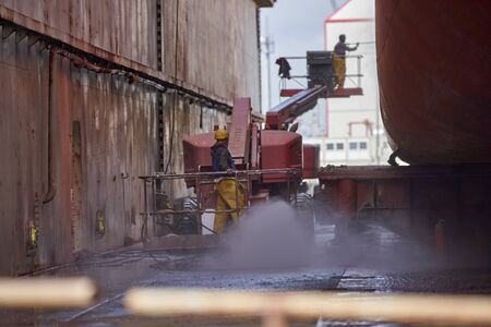 A crane with a worker doing work on ship in background a second worker renew the painting in drydock on a shipyardの写真素材