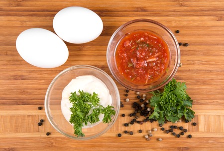 Sauces in bowls and eggs on a wooden board, top viewの写真素材