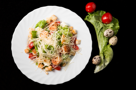 Caesar salad with prawns, cherry tomato and cheese on white plateの写真素材
