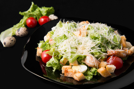 Caesar salad with prawns, cherry tomato and cheese on black plateの写真素材