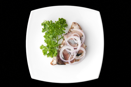 Sandwich with slices herring decorated by onion on white plate on black backgroundの写真素材