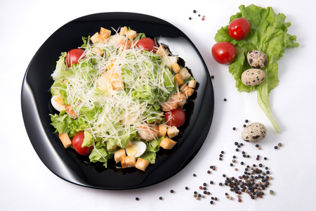 Caesar salad with prawns, cherry tomato and cheese on black plateの写真素材