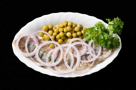 Slices herring with peas, decorated by onion on white plate on black background, top viewの写真素材
