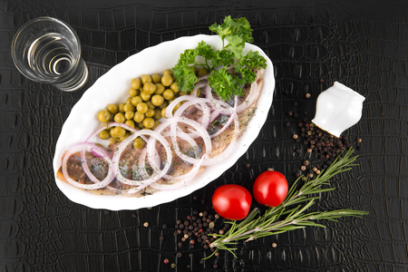 Slices herring with peas, decorated by onion on white plate on black background, top viewの写真素材