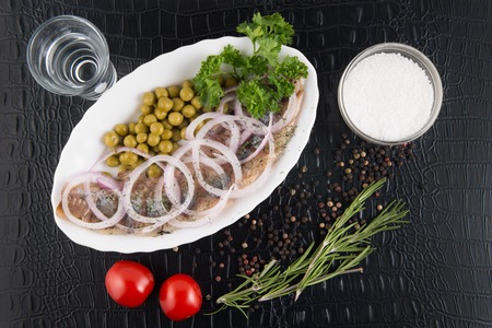 Slices herring with peas, decorated by onion on white plate on black background, top viewの写真素材