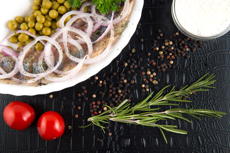 Slices herring with peas, decorated by onion on white plate on black background, top viewの写真素材