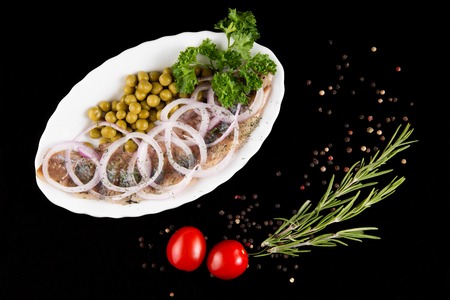 Slices herring with peas, decorated by onion on white plate on black background, top viewの写真素材