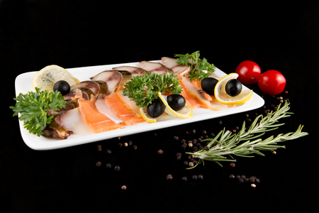 Slices fish, decorated by lemon and olives on white plate on black backgroundの写真素材