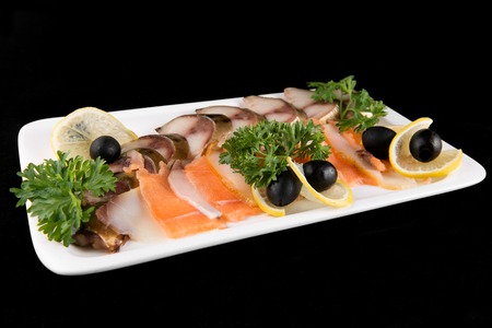 Slices fish, decorated by lemon and olives on white plate on black backgroundの写真素材