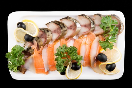 Slices fish, decorated by lemon and olives on white plate on black background top viewの写真素材