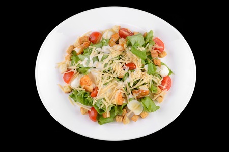 Caesar salad with prawns, cherry tomato and cheese on white plate on black backgroundの写真素材