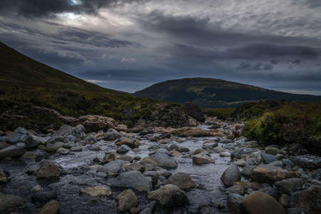 A landscape with a river full of rocks in the foreground and the mountains in the background under a stormy sky, Isle of Skye, Scotland, United Kingdomの写真素材