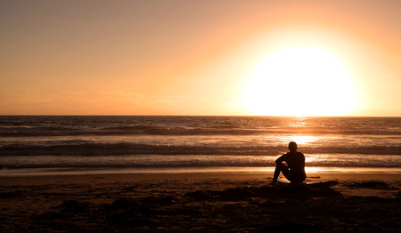 Surfer sitting on surf board on the ocean beach at sunsetの写真素材