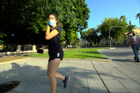 Seville, 23 July 2020 A young lady is jogging in the street. She is wearing a maskのeditorial素材