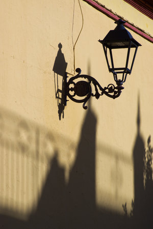 This is a composition with a street lamp and some shadows. Just on a wallof the parish church in...