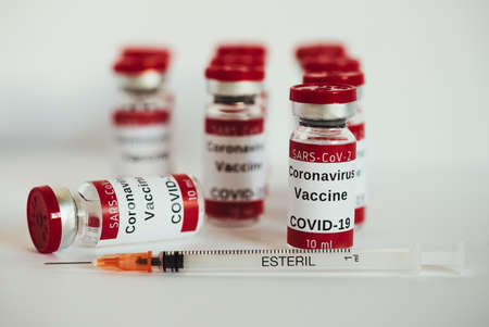 Covid-19 vaccine - coronavirus vaccination bottles. Ten injection vials with red cap on white background. Selective focus on the first vial. Immunization treatment. Bottles of ten milliliters.の写真素材